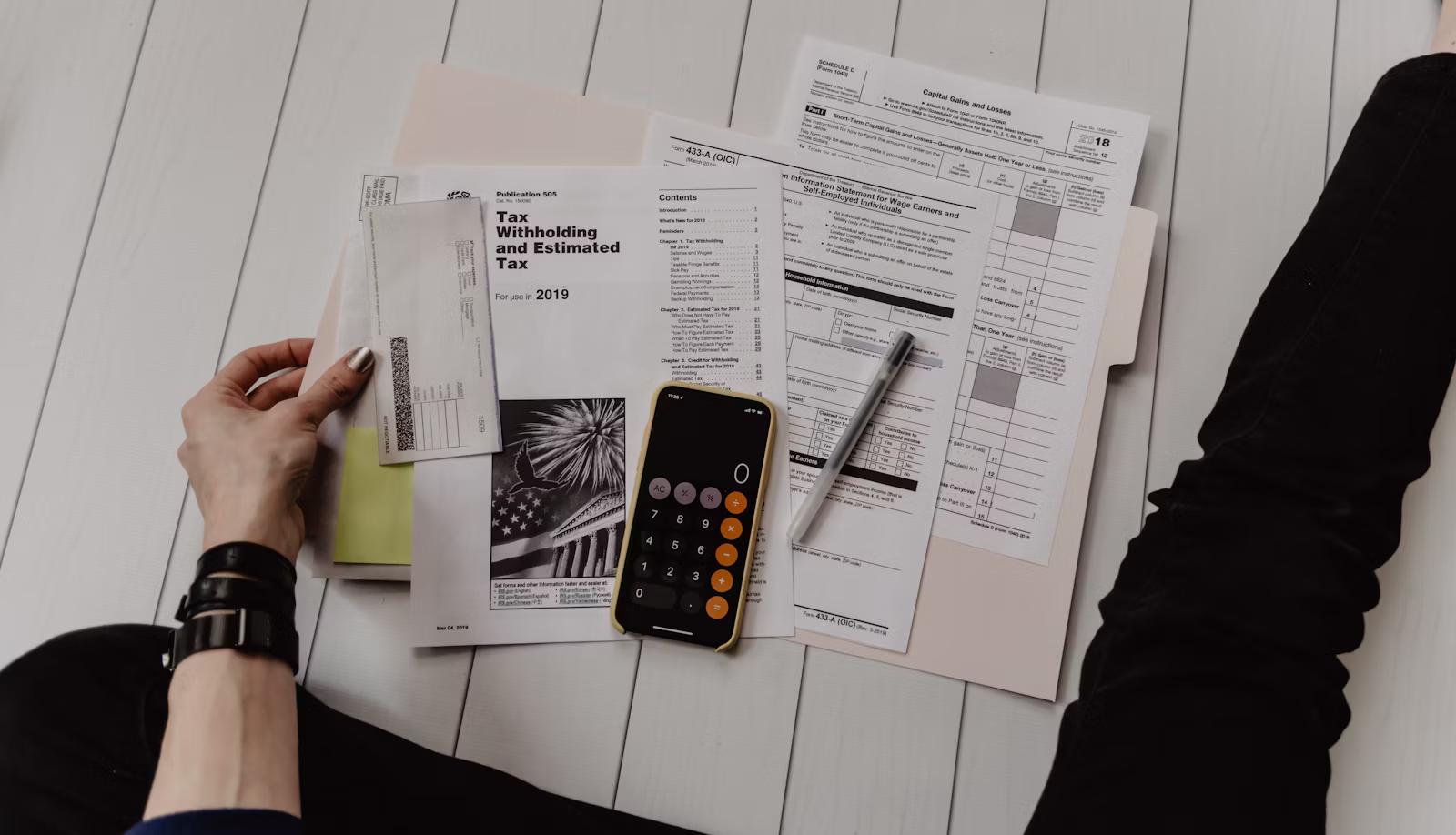 Calculator and notepad on a desk beside a laptop, working out a budget