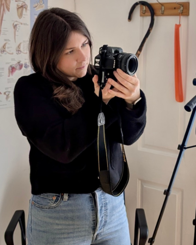 Person adjusting a DSLR camera during a content shoot in a clinical setting, with anatomical posters and a tripod in the background.